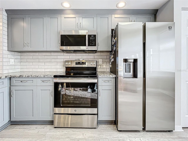 kitchen with gray cabinets, decorative backsplash, light stone countertops, and stainless steel appliances