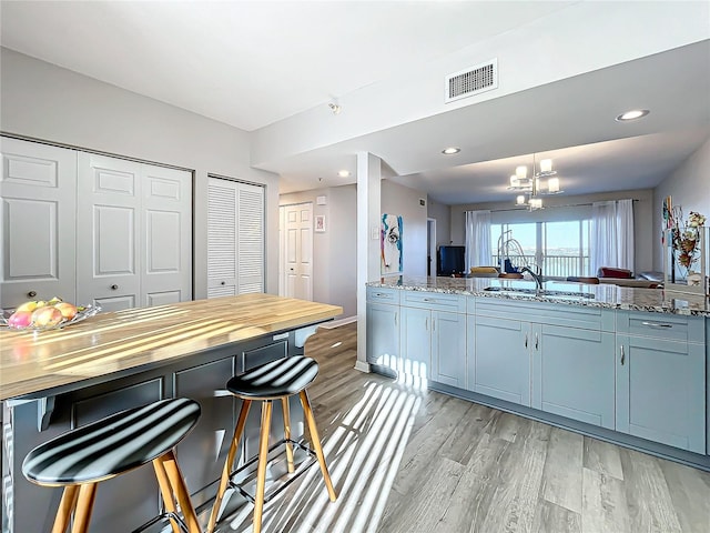 kitchen featuring light hardwood / wood-style flooring, light stone countertops, sink, and an inviting chandelier