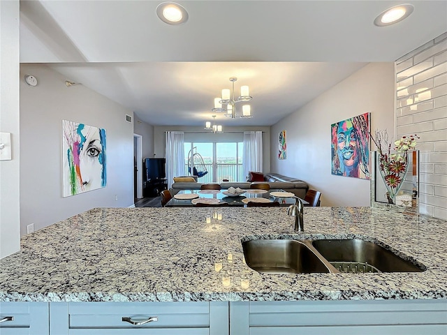 kitchen with an inviting chandelier, sink, light stone countertops, and white cabinetry