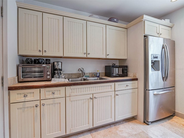 kitchen with butcher block countertops, sink, stainless steel fridge with ice dispenser, and cream cabinets