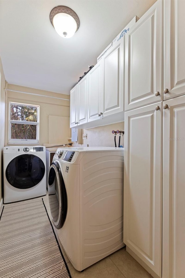 clothes washing area featuring cabinets, light tile patterned flooring, and washing machine and clothes dryer