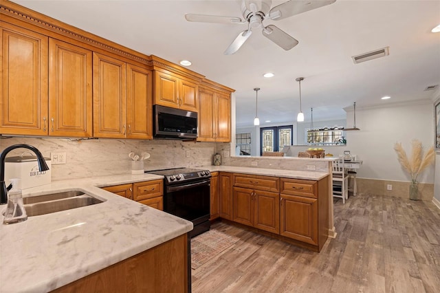 kitchen featuring decorative light fixtures, stainless steel appliances, brown cabinetry, a sink, and a peninsula