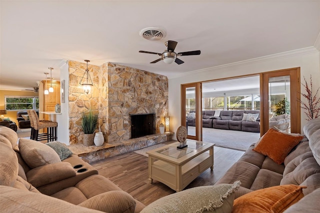 living room featuring visible vents, light wood-style floors, ornamental molding, ceiling fan, and a stone fireplace