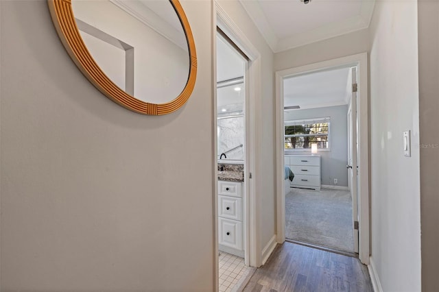 hallway featuring baseboards, light wood-style floors, and crown molding