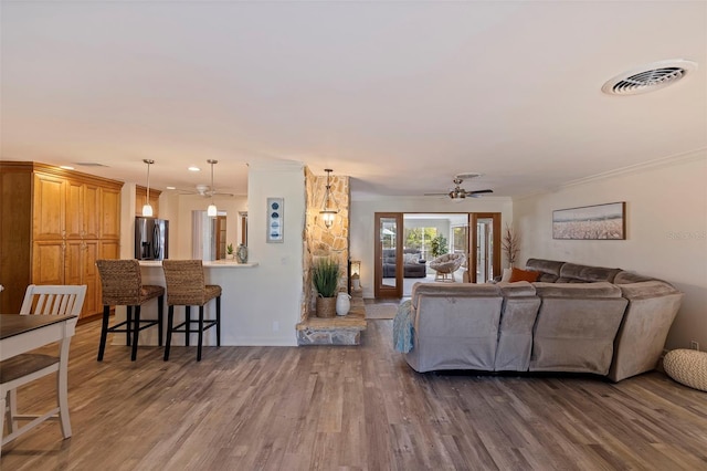 living area with a ceiling fan, crown molding, visible vents, and dark wood-type flooring