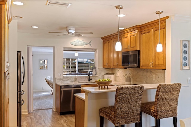 kitchen with stainless steel appliances, light countertops, brown cabinetry, a peninsula, and a kitchen breakfast bar