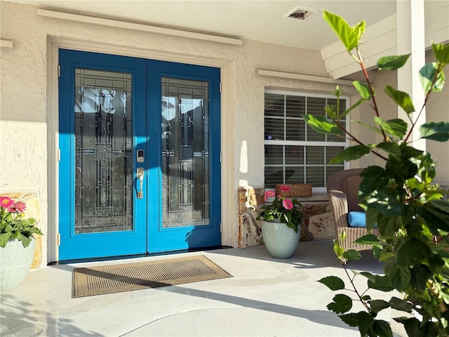 entrance to property featuring stucco siding, visible vents, and french doors