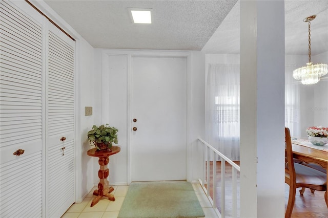 hall with a notable chandelier, a textured ceiling, and light tile patterned floors