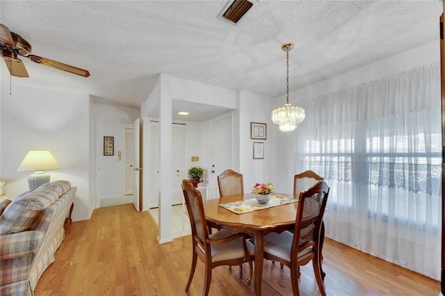 dining space featuring light hardwood / wood-style flooring, a textured ceiling, and ceiling fan with notable chandelier