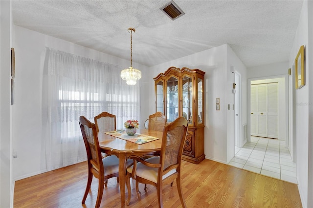 dining area with a chandelier, light hardwood / wood-style flooring, and a textured ceiling