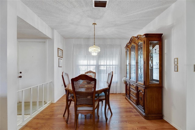 dining space with light hardwood / wood-style floors, a textured ceiling, and a chandelier