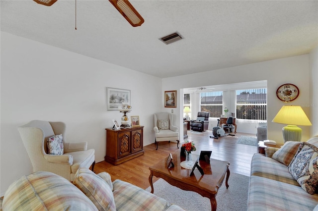 living room with light hardwood / wood-style flooring, a textured ceiling, and ceiling fan