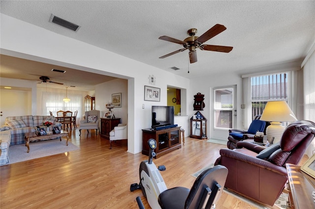 living room featuring a textured ceiling, light wood-type flooring, and ceiling fan