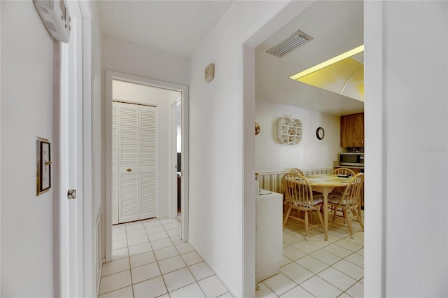 corridor with a textured ceiling, a wall mounted air conditioner, and light tile patterned floors