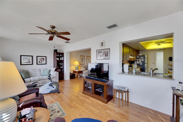 living room featuring ceiling fan, a textured ceiling, and light wood-type flooring