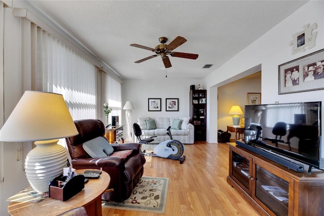 living room featuring a textured ceiling, light wood-type flooring, and ceiling fan