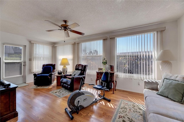 living room with a textured ceiling, light wood-type flooring, and ceiling fan