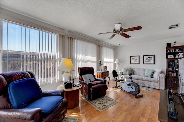 living room with ceiling fan, a textured ceiling, and light hardwood / wood-style flooring