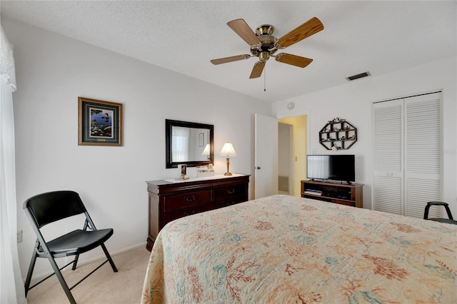 bedroom with a closet, light carpet, a textured ceiling, and ceiling fan