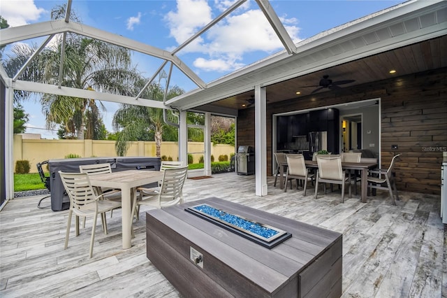 wooden terrace featuring an outdoor fire pit, ceiling fan, a grill, and glass enclosure