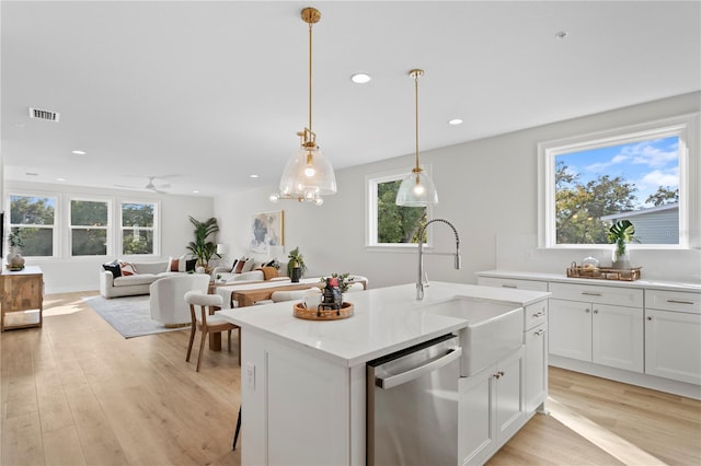 kitchen with stainless steel dishwasher, a kitchen island with sink, ceiling fan, sink, and white cabinetry