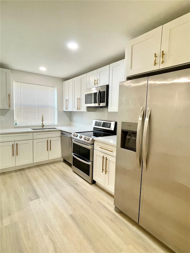 kitchen with appliances with stainless steel finishes, sink, light wood-type flooring, and white cabinets