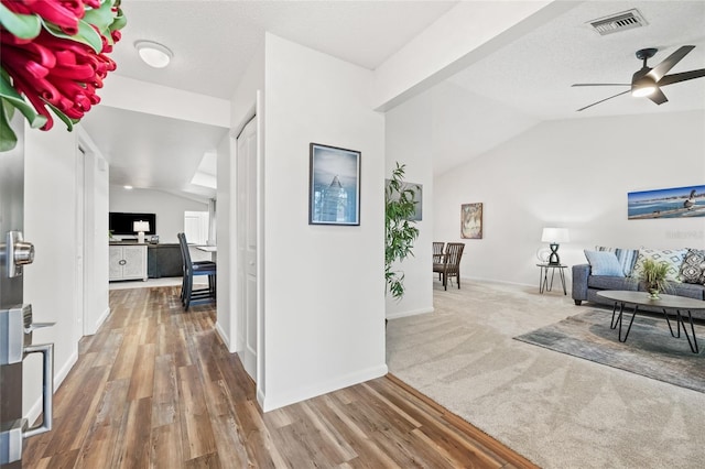 hall featuring hardwood / wood-style flooring, vaulted ceiling, and a textured ceiling