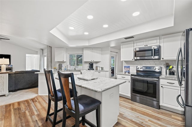 kitchen with appliances with stainless steel finishes, a center island, white cabinets, and light hardwood / wood-style floors