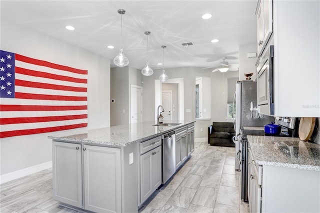 kitchen with sink, hanging light fixtures, ceiling fan, stainless steel appliances, and a center island with sink