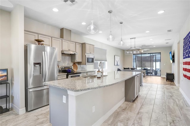 kitchen with gray cabinetry, sink, stainless steel appliances, light stone counters, and a kitchen island with sink