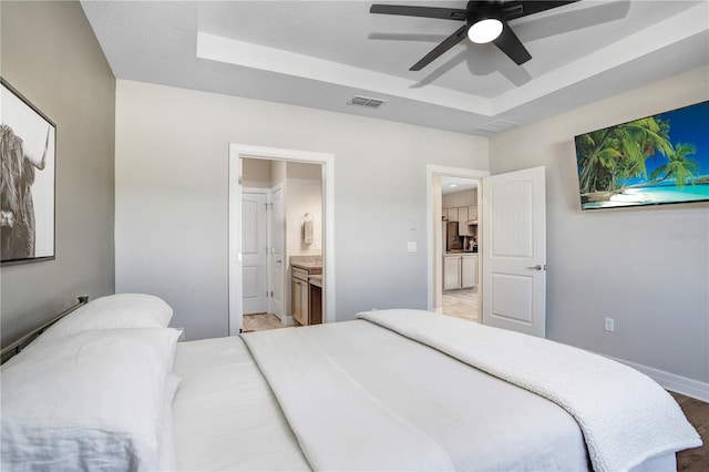 bedroom with light hardwood / wood-style flooring, ensuite bathroom, a tray ceiling, and ceiling fan