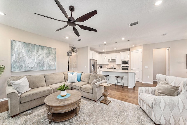 living room with light hardwood / wood-style floors, a textured ceiling, and ceiling fan