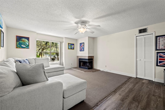 living room with ceiling fan, wood-type flooring, a textured ceiling, and a fireplace