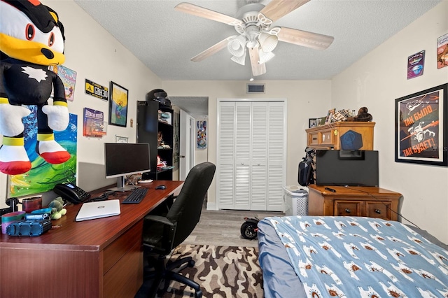 bedroom with light hardwood / wood-style floors, a textured ceiling, a closet, and ceiling fan