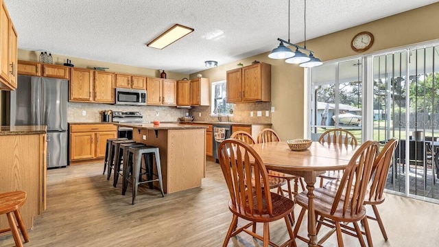 kitchen with tasteful backsplash, hanging light fixtures, a kitchen island, appliances with stainless steel finishes, and light hardwood / wood-style floors