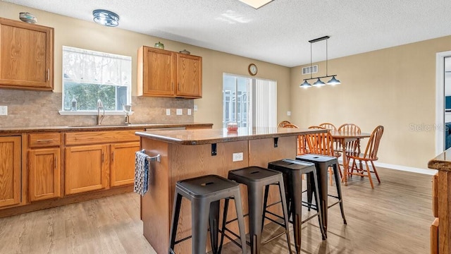 kitchen featuring hanging light fixtures, a breakfast bar, light hardwood / wood-style flooring, sink, and a center island