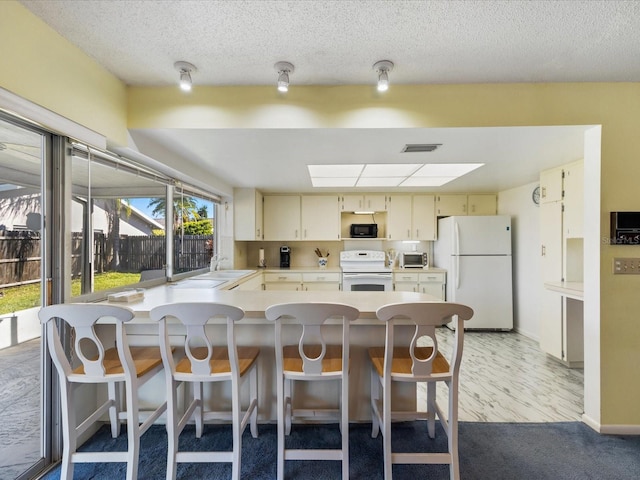 kitchen with white appliances, a healthy amount of sunlight, cream cabinets, and a kitchen breakfast bar