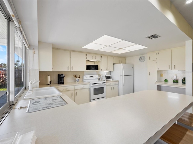 kitchen featuring white appliances, cream cabinets, sink, a kitchen bar, and decorative backsplash