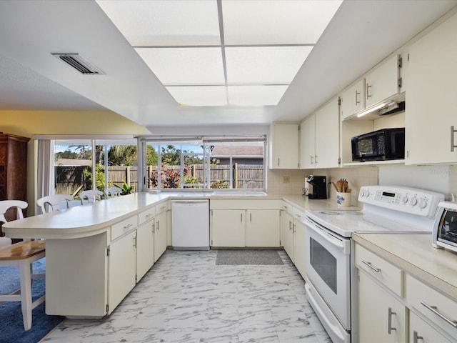 kitchen featuring kitchen peninsula, white cabinets, tasteful backsplash, a kitchen bar, and white appliances