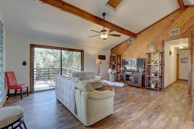 living room featuring lofted ceiling with beams, wood walls, wood finished floors, and visible vents