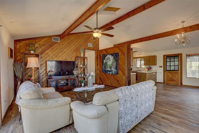 living room featuring vaulted ceiling with beams, wood walls, wood finished floors, and visible vents