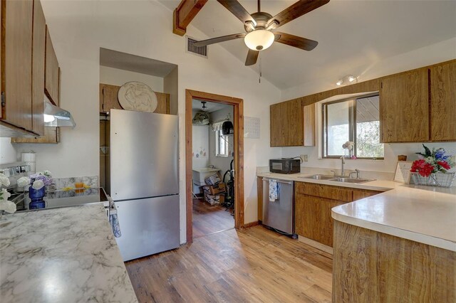 kitchen featuring stainless steel appliances, a sink, vaulted ceiling, light countertops, and brown cabinets