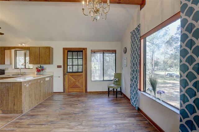 kitchen with brown cabinetry, a sink, light countertops, light wood-style floors, and a notable chandelier