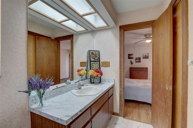 bathroom with a skylight, a ceiling fan, ensuite bath, marble finish floor, and vanity