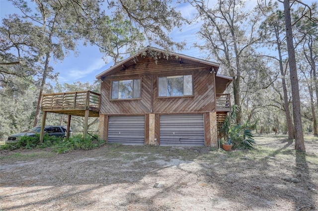 view of property exterior with dirt driveway, a wooden deck, and a garage