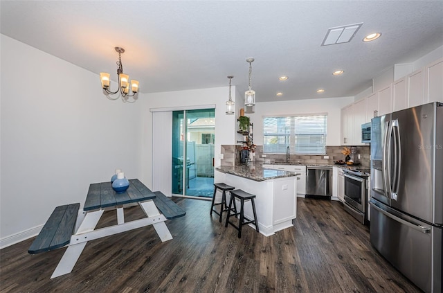 kitchen featuring white cabinets, hanging light fixtures, dark hardwood / wood-style flooring, a kitchen bar, and stainless steel appliances