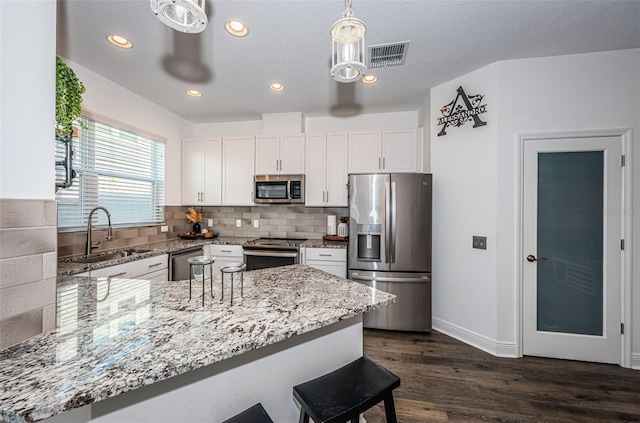 kitchen with kitchen peninsula, stainless steel appliances, sink, decorative light fixtures, and white cabinets