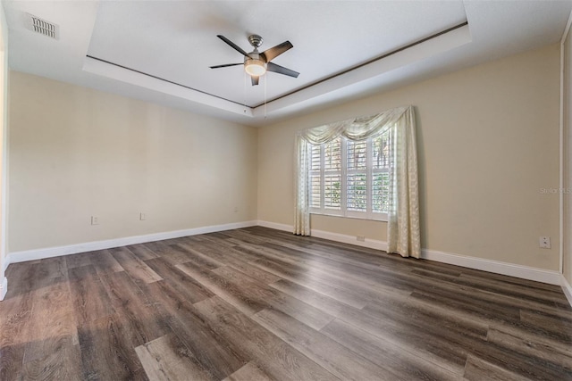 empty room with ceiling fan, a tray ceiling, and dark hardwood / wood-style flooring