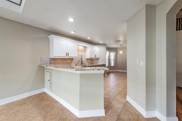 kitchen featuring light stone counters, light tile patterned flooring, kitchen peninsula, and white cabinets