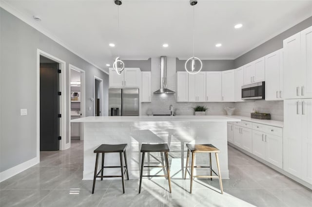 kitchen with pendant lighting, white cabinets, wall chimney range hood, appliances with stainless steel finishes, and a kitchen island